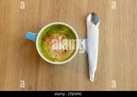 Blaue Tasse mit grünem Tee Matcha Latte, mit gefriergetrockneten Erdbeeren, Löffel auf Holztisch, Kopierplatz. Gesundes Ernährungskonzept, Getränke mit vegetab Stockfoto