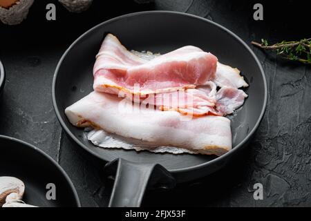 Brutzelnde Speckstücke in gusseiserner Bratpfanne auf schwarzem Hintergrund Stockfoto