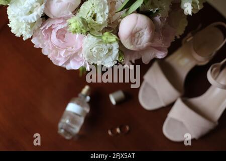 Brautstrauß aus weißen Rosen und Pfingstrosen mit Brautschuhen Und Eheringe auf dem Tisch vor der Trauung Stockfoto