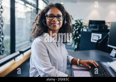 Porträt einer selbstbewussten Führungskraft, die im Büro ein Headset trägt. Geschäftsfrau mit Headset, die in die Kamera blickt und lächelt. Stockfoto