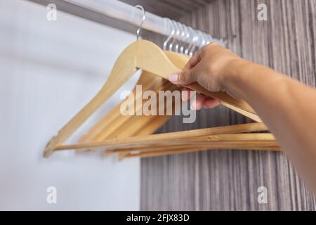 Kleiderbügel aus Holz in einem leeren offenen Schrank, die Hand nimmt einen Kleiderbügel Stockfoto