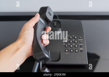 Telefon in einem Hotelzimmer, Hand mit einem erhöhten Telefonhörer aus der Nähe Stockfoto
