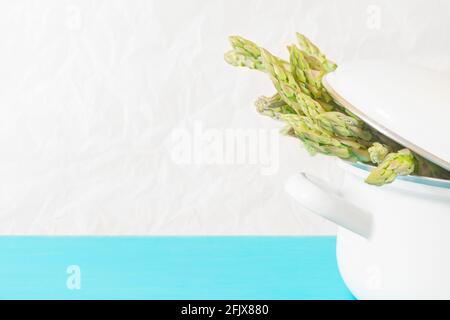 Hintergrund mit grünem Spargel in einem weißen Topf auf einem Heller Hintergrund Stockfoto
