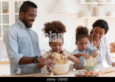 Lustige afroamerikanische Eltern helfen niedlichen Kindern, Teig zu kneten Stockfoto