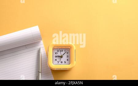 Gelbe Uhr und Notizblock auf gelber Tischplatte. Speicherplatz kopieren. Stockfoto