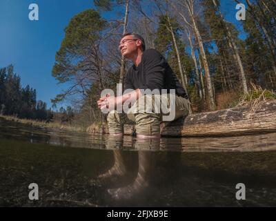 Mann hält die Füße im klaren Wasser des Sees und genießt es Natur Stockfoto