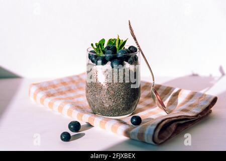 Chia Pudding mit Creme und Heidelbeeren auf Stoffserviette auf weißem Tisch. Gesundes veganes Essen. Vorderansicht. Stockfoto
