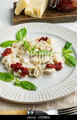 Ravioli-Pasta mit Pilzsahnesauce und Käse: Italienische Küche mit Basilikum-Parmesan und Tomaten auf weißem Teller auf weißem Hintergrund Stockfoto