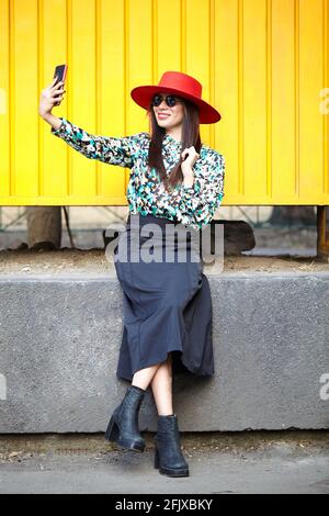 Stylische junge hispanische Frau, die ein Selfie auf einem Gelb nimmt Wand Stockfoto
