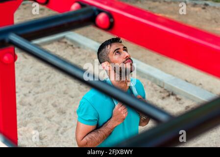 Draufsicht auf einen bärtigen, brünetten Sportler mit einem Handtuch um den Hals auf den Calisthenics-Bars. Fitnesskonzept im Freien. Stockfoto