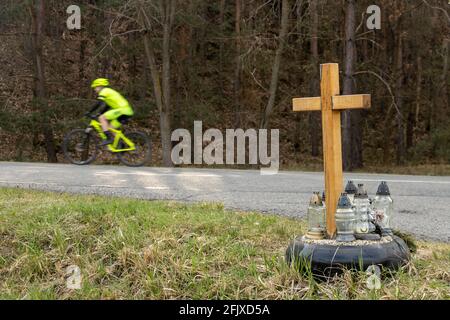 Ein Kreuz am Straßenrand mit Kerzen zum Gedenken an den tragischen Tod, auf einer Fahrt im Hintergrund verschwommen Radfahrer. Stockfoto