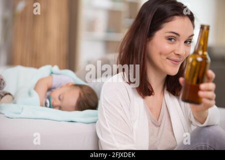 Mutter trinkt Bier, während sie im Hintergrund in der Bucht schläft Stockfoto