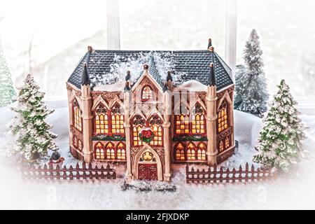 Wunderschönes Gebäude mit Buntglasfenstern und dekorativen Türmen Weihnachtsdorf im Fenster mit Schnee und immergrünen eingerichtet Bäume Stockfoto
