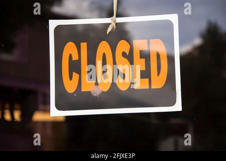 Geschlossenes Schild, das an einer Schnur im Geschäftsfenster hängt - Krumm mit Klebstoff, der es auch am Fenster befestigt - einige abstrakte Reflexionen Stockfoto