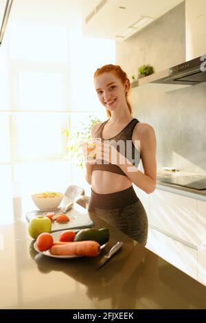 Athletische Frau mit Turnkleidung trinkt Orangenfrüchte in der Küche Stockfoto