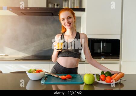 Athletische Frau mit Turnkleidung trinkt Orangenfrüchte in der Küche Stockfoto