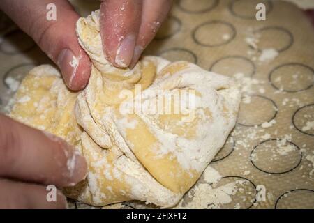 Hände verdrehen den Knopf des Teiges auf einem Krinkali-Knödel Mit Mehl auf einer Silikonmatte bedeckt - selektiver Fokus Stockfoto