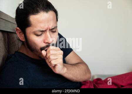 Junger lateinischer Mann, der zu Hause krank auf dem Bett hustet Stockfoto