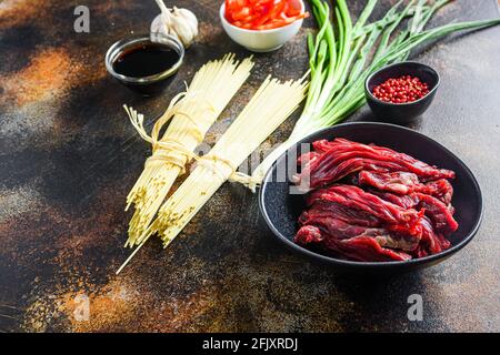 Rohzutaten zum Rühren Chinesische Nudeln mit Gemüse und Rindfleisch in einer schwarzen Schüssel anbraten. Auf alten rustikalen Tisch. Seitenansicht. Stockfoto