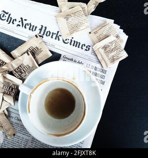 Eine schmutzige Tasse Kaffee, leer mit Kaffeemarken, die auf der New York Times Zeitung sitzen, und Zuckerpakete von Sugar im Rohkost umgeben sie Stockfoto