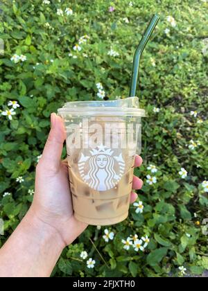 Das Halten eines Glashalms in einer Starbucks Kaffeetasse sollte die Notwendigkeit von Einweg-Plastikhalmen reduzieren, indem wiederverwendbare Strohhalme verwendet werden. Grünes Gras Hintergrund Stockfoto