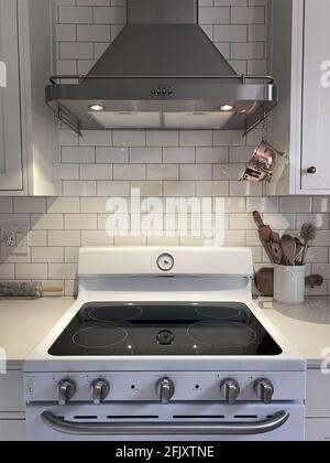Weißer Küchenschrank mit U-Bahn-Fliesen. Küchenutensilien befinden sich in einer Schüssel zum Kochen mit einem kleinen Vintage-Kupfer-Sieb zum Aufhängen. Dunstabzugshaube in der Küche. Stockfoto