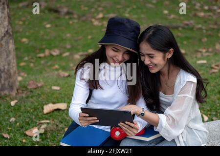 Zwei Studentinnen der Universität studieren im Freien und nutzen zusammen im Park der Universität ein digitales Tablet Stockfoto