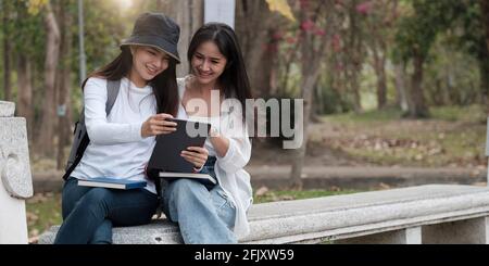 Zwei Studentinnen der Universität studieren im Freien und nutzen zusammen im Park der Universität ein digitales Tablet. Stockfoto
