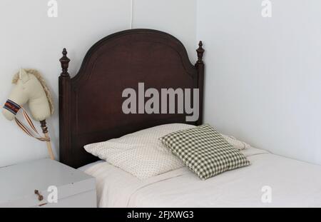 Kinderzimmer. Bettgestell aus Holz mit kleiner Wandlampe über der Wand zum Lesen in der Nacht. Ein Spielpferd auf einem Stock sitzt neben dem Bett und Vintage Spielzeug ch Stockfoto