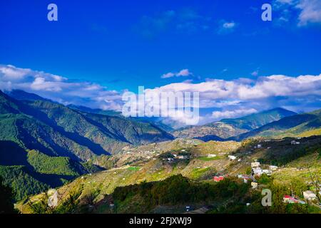 Rot überdachte Häuser im Tal. Berge unter dem blauen Himmel und weißen Wolken. Verschiedene Pflanzenarten und Naturlandschaften. Wuling Farm im Winter, T Stockfoto