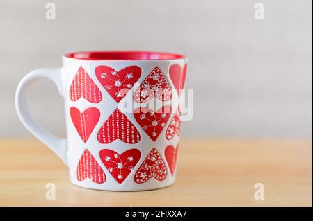 Weiße Tasse auf Holzhintergrund. Becher mit herzförmigen Mustern auf unscharfem Hintergrund Stockfoto