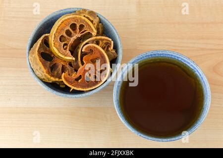 Sonnengetrocknete Bael-Früchte in Schale neben einer Tasse heißen Bael-Kräutertee, auch Steinapfel genannt, Draufsicht auf Holzhintergrund (Aegle Marmelos) Stockfoto