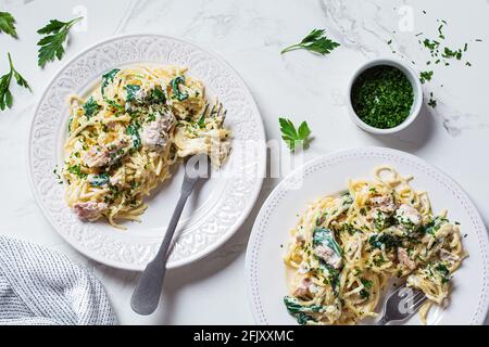 Spaghetti mit Thunfisch, Spinat und cremiger Sauce auf einem weißen Teller mit Kräutern, weißem Marmorboden. Stockfoto