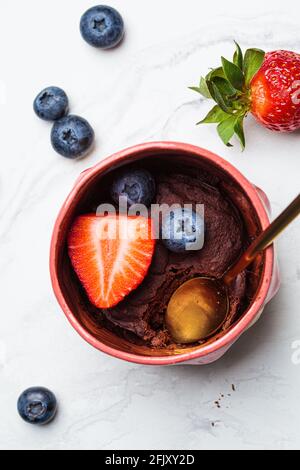 Schokoladen-Becher-Kuchen mit Beeren in einem rosa Becher auf weißem Marmorboden. Schnelle vegane Mikrowelle Rezept. Stockfoto