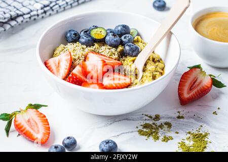 Matcha-Haferflockenschale mit Beeren und Ahornsirup auf weißem Marmorboden. Gesundes Frühstück, veganes Essen, Detox-Rezept. Stockfoto