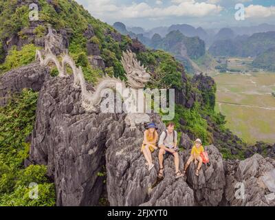 Familie von Touristen auf dem Hintergrund der erstaunlichen riesigen Drachenstatue auf Kalkstein Berggipfel in der Nähe Hang Mua Aussichtspunkt am nebligen Morgen. Beliebt Stockfoto