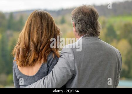 Ein liebendes Paar mittleren Alters, das vom Balkon aus aufstand und hinüberblickte Ländliche Landschaft in einer Nahaufnahme Rückansicht mit dem Ehemänner bewaffnen sich um seine Frau Stockfoto