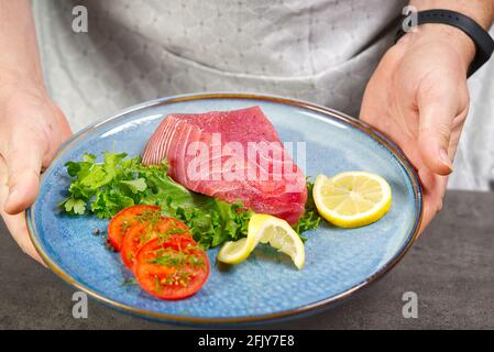 Rohes Thunfischsteak mit Salat und Zitrone auf blauem Teller. Man Holdin Gplate mit Thunfischsteak. Lifestyle, gesunde Ernährung, Kochen und Diät-Konzept. Stockfoto