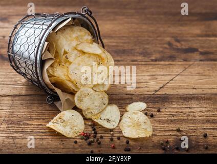 Kartoffelchips Chips mit schwarzem Pfeffer in Stahl-Snack-Eimer auf Holztisch Hintergrund. Bester Snack für Bier und Limonade. Stockfoto