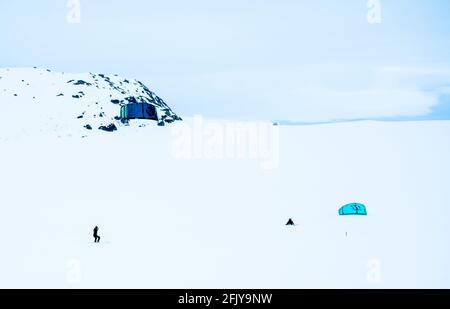 Menschen Snowkiten auf einer gefrorenen schneebedeckten Bergebene an einem kalten Wintertag. Stockfoto
