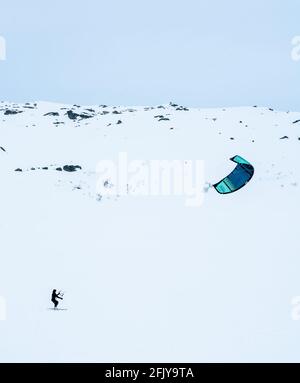 Menschen Snowkiten auf einer gefrorenen schneebedeckten Bergebene an einem kalten Wintertag. Stockfoto