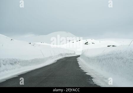 Straße durch einen Bergpass mit tiefem Schnee, der auf beiden Seiten aufragt. Stockfoto