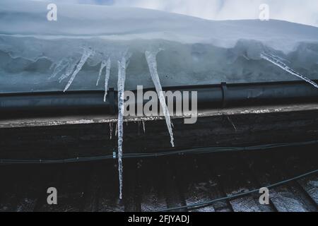 Lange spitzen Eiszapfen aus gefrorenem Wasser, das an der Seite eines Daches hängt. Stockfoto