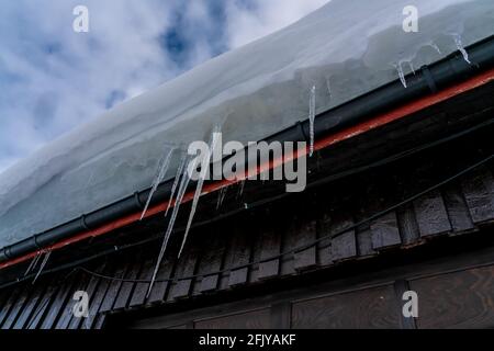 Lange spitzen Eiszapfen aus gefrorenem Wasser, das an der Seite eines Daches hängt. Stockfoto