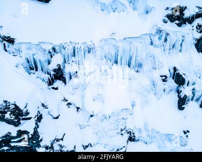 Massive lange gefrorene Eiszapfen, die an der Seite einer Klippe auf einer Bergseite hängen. Stockfoto
