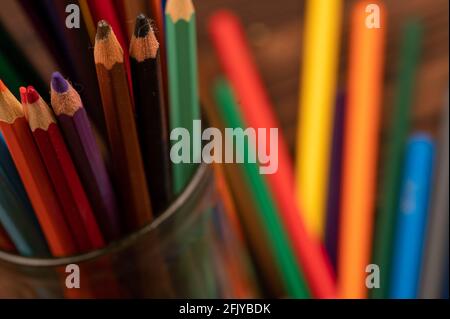 Bunte Bleistifte in einem Glas und auf einem Holztisch verstreut. Nahaufnahme mit selektivem Fokus. Stockfoto