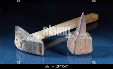 Hammer und Amboss zum Stanzen der Sense auf dem Tisch. Ein rostiger Gegenstand auf schwarzem Hintergrund Stockfoto