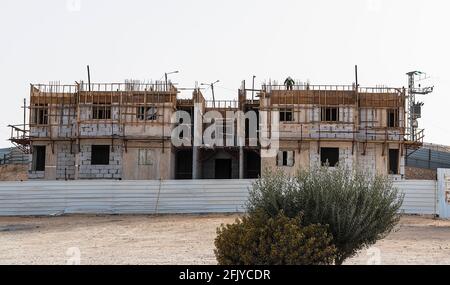 Ein Inspektor auf einem Betonblock darunter Bau in Mitzpe Ramon in Israel hinter einer Metallbarriere Zaun mit Sträuchern Stockfoto