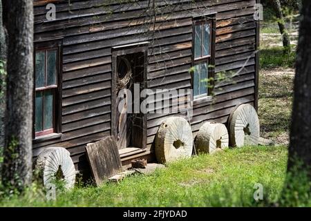 Opelika, Alabama, USA - 7. April 2021: Alte Mühlsteine lehnen sich an die historische Bean's Mill, die sich am Halawakee Creek im ländlichen Lee County im Spri befindet Stockfoto
