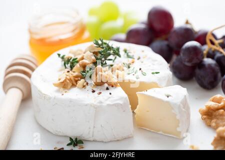 Brie- oder Camembert-Käse mit Trauben, Walnüssen und Honig auf Käseplatte aus weißem Marmor Stockfoto